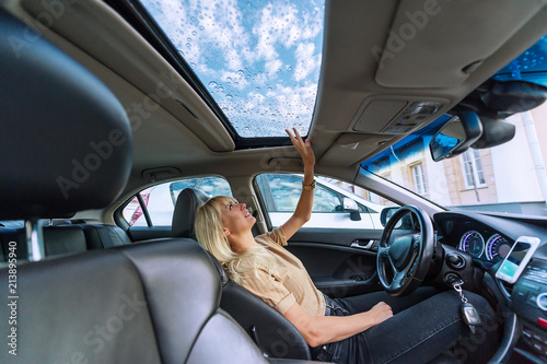Blonde woman in modern car. Raindrops on a glass roof of the car photo