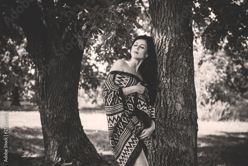 Gypsy girl with long hair posing at nature. A woman with a slim figure and athletic body in knitted sweater, dressed in a sexy kardigan, vintage tones 