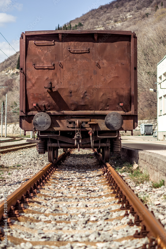 Industrial view of the back of a brown vagon covered with rust. Vagon standing on rails.