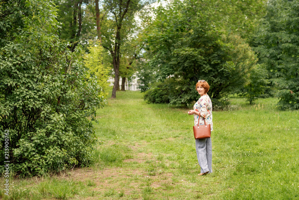 a red-haired, middle-aged woman walking along the grassy green path in the park and looking back a red-haired, middle-aged woman walking along the grassy green path in the park and looking back