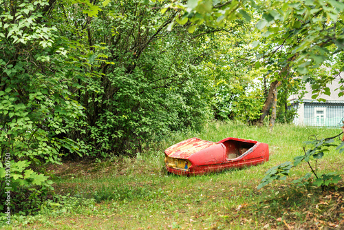 shabby abandoned old broken machine from the carousel in the green of the park trees