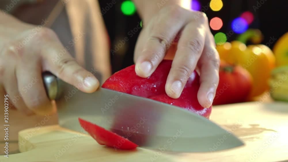 Close-up of asian woman cutting bell pepper on wood board in kitchen at home, sliding shot