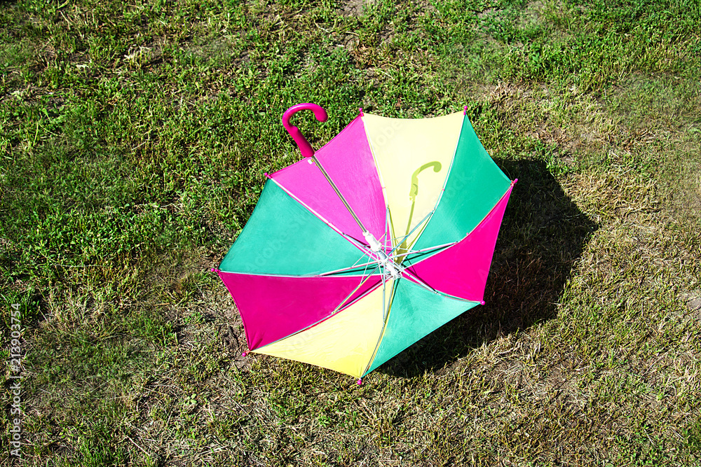 a colored children's umbrella lies on the green grass in the garden
