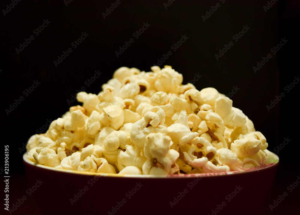 golden popcorn tub closeup with butter popcorn in it in front of black background golden popcorn tub closeup with butter popcorn in it in front of black background