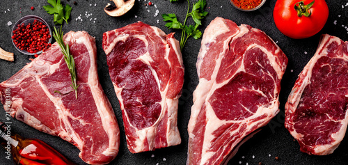 Meat raw steaks lie on a black background with vegetables, tomatoes, marasmade, mushrooms. background image. side view, copy space, top view photo
