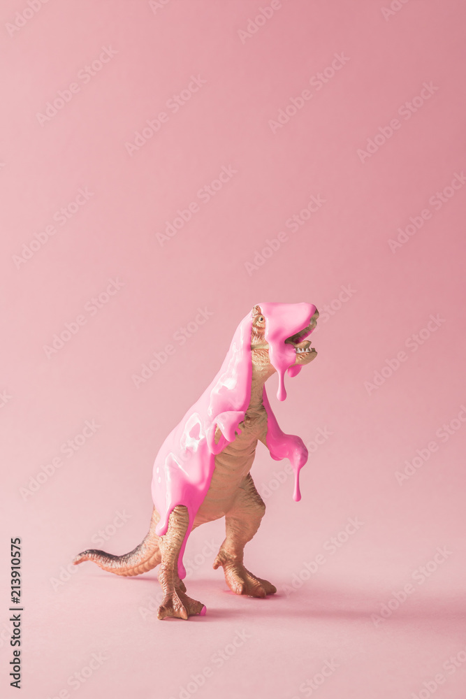 Obraz premium Różowa farba kapiąca na zabawkę dinozaura. Kreatywna koncepcja minimalna.