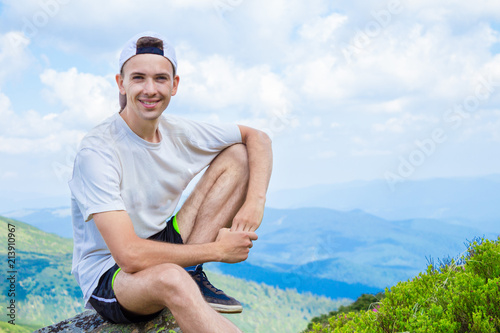 man hiker relaxing on top of hill and admiring beautiful mountain valley view in summer day