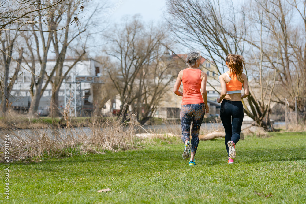 Mother and adult daughter running for sport along the river for better fitness Mother and adult daughter running for sport along the river for better fitness