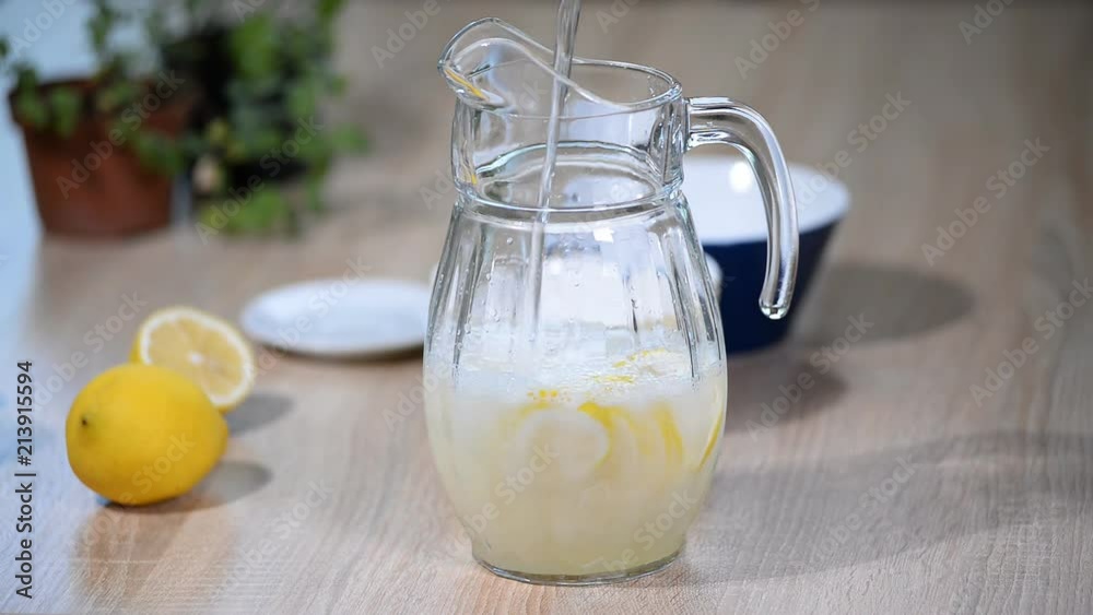 In a jug of lemons pour water. Glass of sparkling water soda drink lemonade with ice and lime lemon slice on white background.