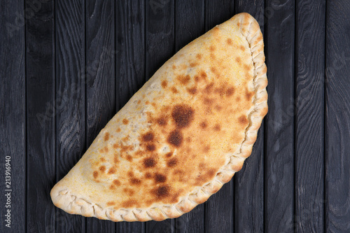 Slika na platnu Fresh baked pizza calzone on dark wooden table, top view.