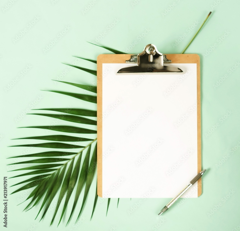 Mock up with clipboard, palm leaf and a pen on pale mint green background. Flat lay, top view.Copy space Mock up with clipboard, palm leaf and a pen on pale mint green background. Flat lay, top view.Copy space