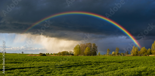 a beautiful, colorful rainbow against the background of a dangerous, stormy sky over a rural farm