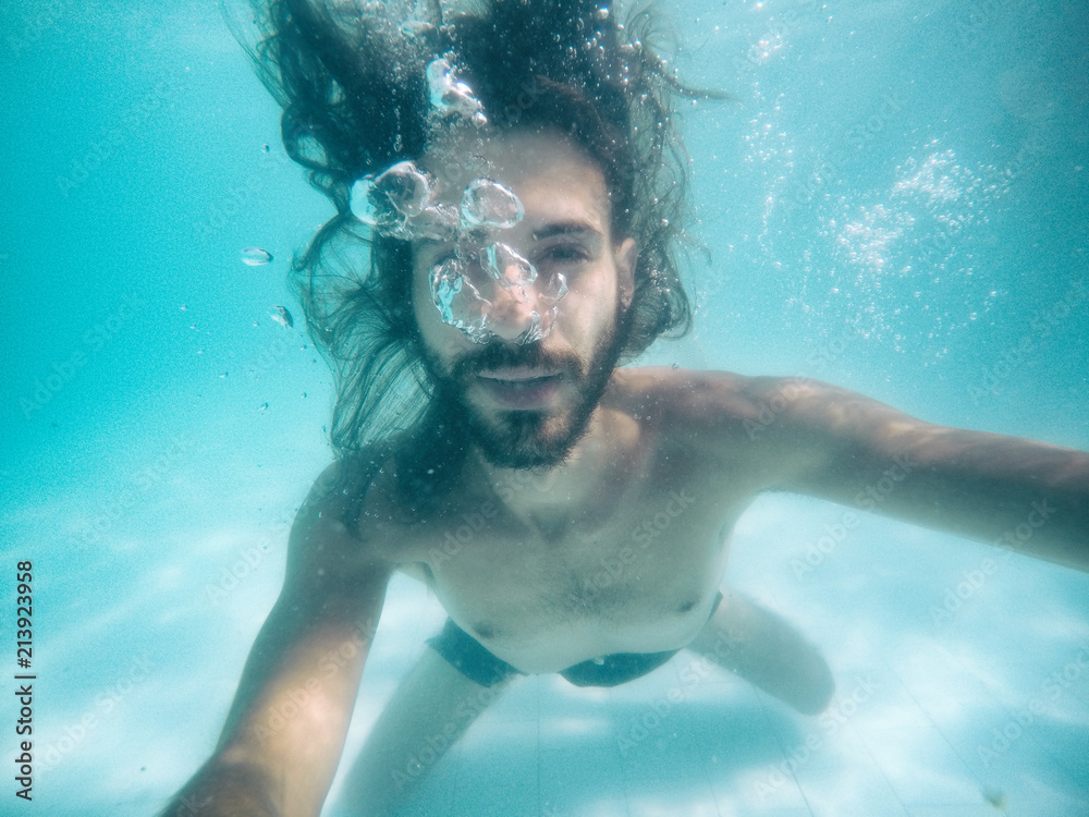 Attractive young man submerged in pool looking at camera