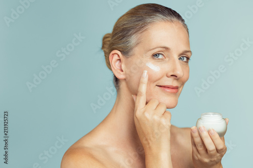 Mature woman applying skin cream on face photo
