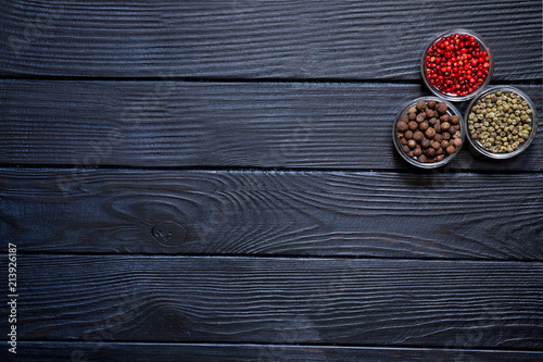 Assortment of different kinds of pepper, red, green and allspice on rustic wooden black background. Spicy ingredeints, asian, mexican  and indian cuisine. Free copy space. photo