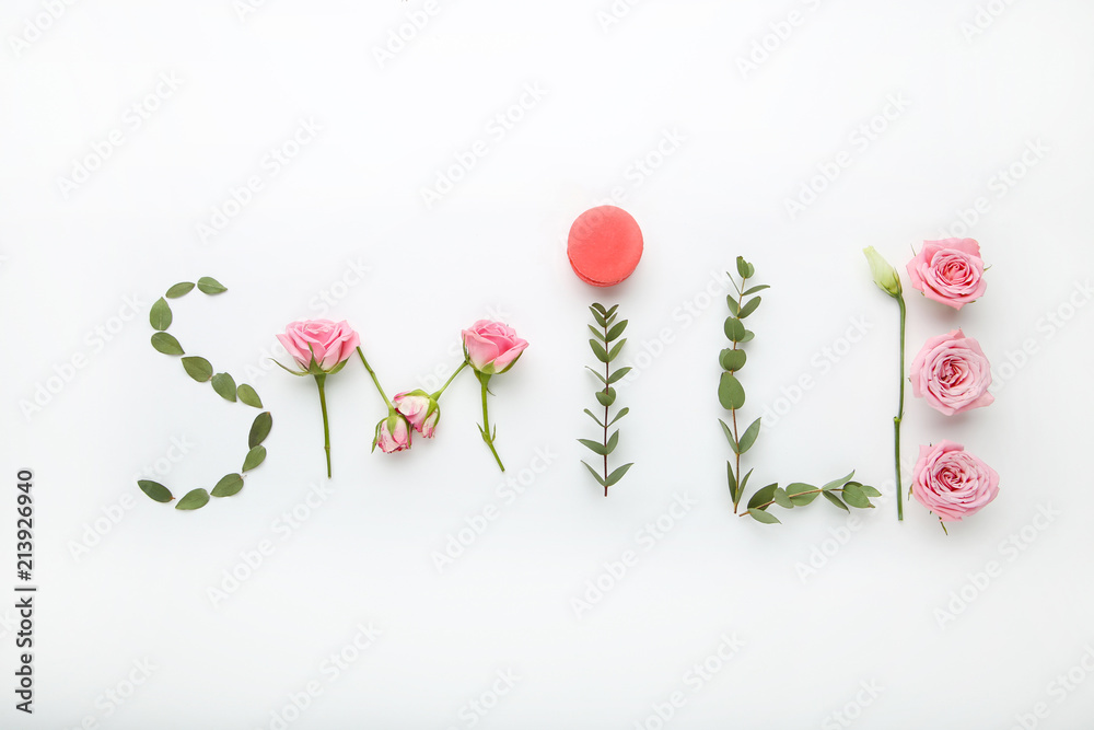 Inscription Smile by flowers and green leafs on white background