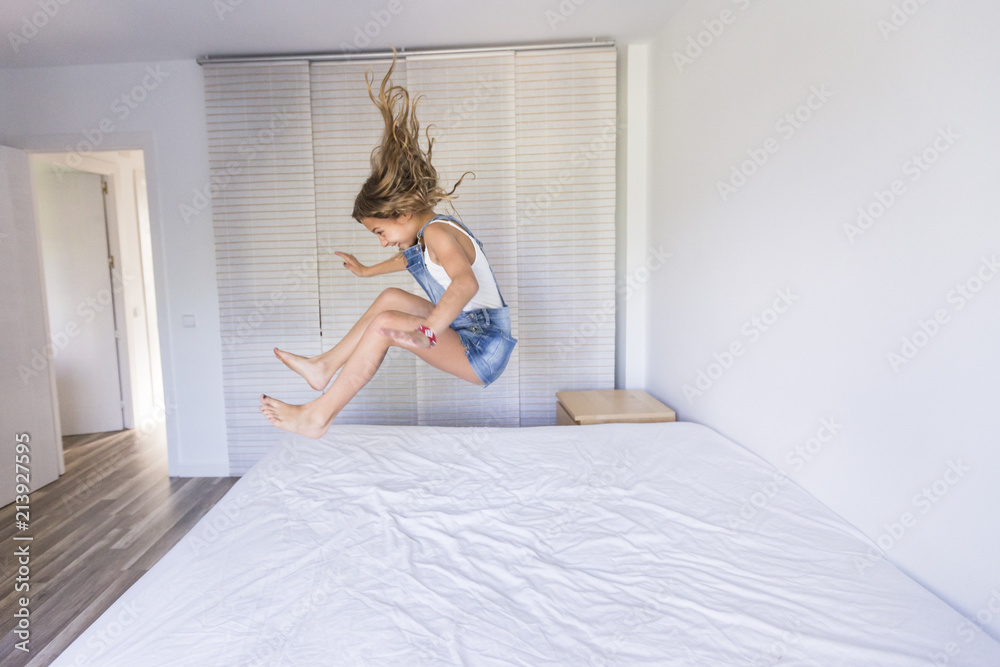 beautiful kid girl playing and jumping on bed. Fun indoors. Family love and lifestyle