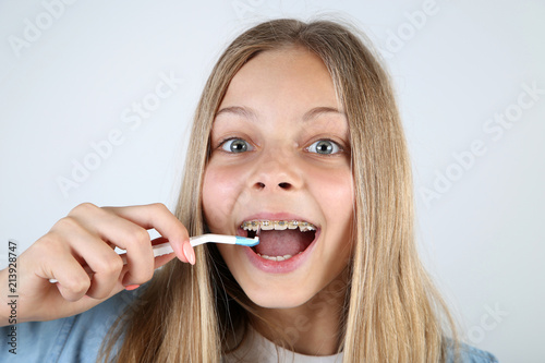 Young smiling girl with dental braces and toothbrush on grey background