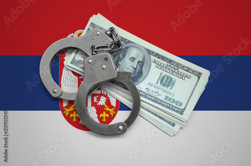 Serbia flag  with handcuffs and a bundle of dollars. Currency corruption in the country. Financial crimes photo