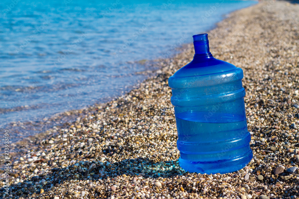 a large water bottle stands on the beach, a large water bottle stands on the beach,