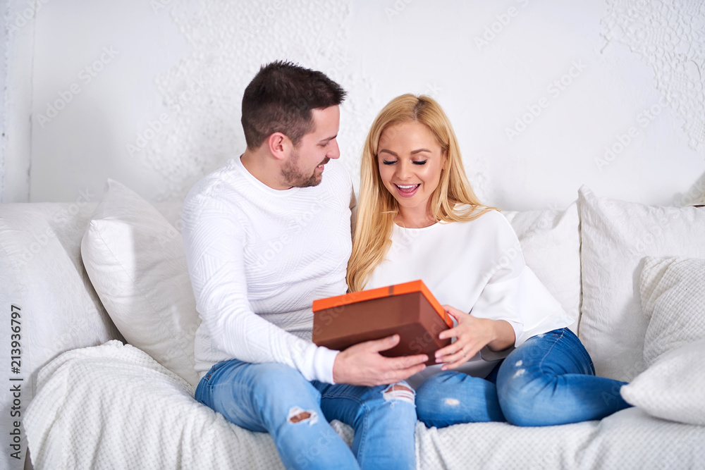 A beautiful happy young couple sitting on the sofa in the living room at christmas and giving presents to each other.