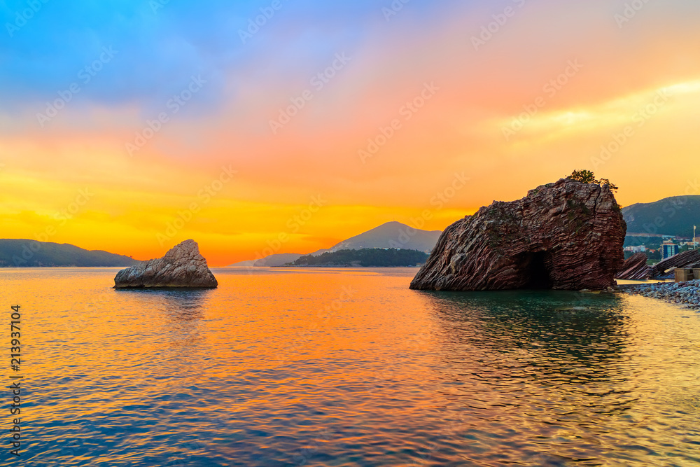 Awesome colorful sunset on the Adriatic sea near Budva city in Montenegro, gorgeous seascape with big rock in the beach