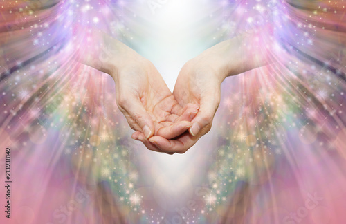 Energy healer receiving high vibrational energy - female cupped hands and shaft of white light against an angelic pink and sparkle energy flow background
