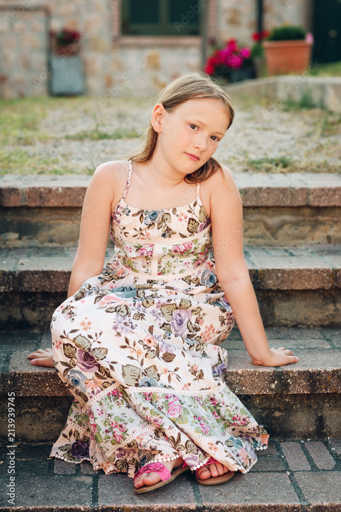 Summer portrait of cute little girl wearing long dress, sitting on stairs