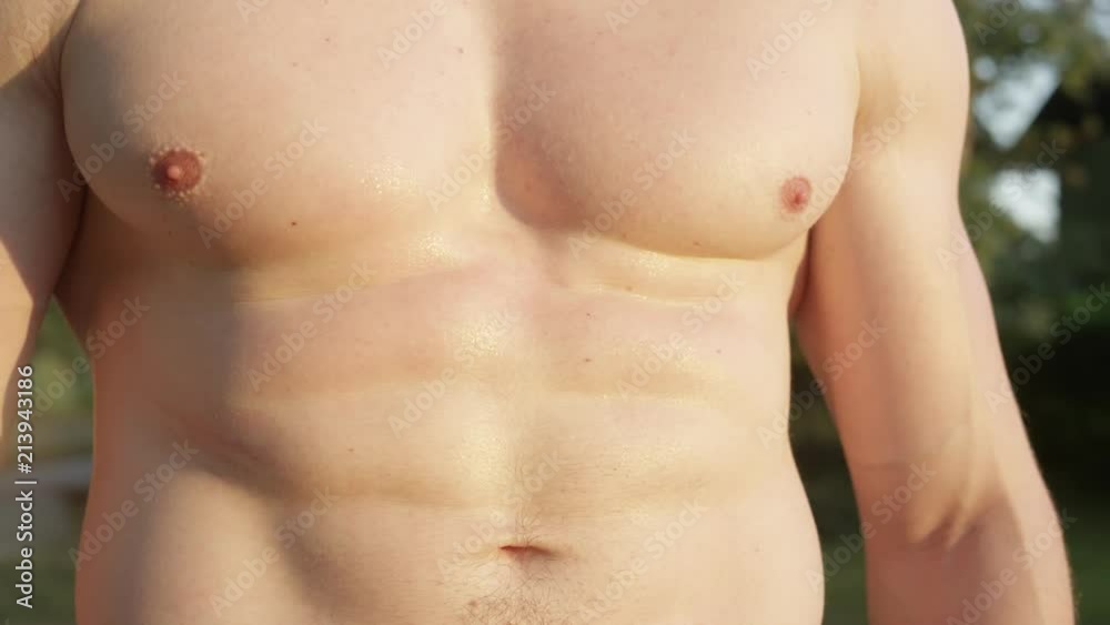 CLOSE UP: Unrecognizable fit male flexes his abdomen after hard exercise in the sunny park. Shirtless man showing off his abs after working out outdoors on a hot summer afternoon. Muscular sportsman. CLOSE UP: Unrecognizable fit male flexes his abdomen after hard exercise in the sunny park. Shirtless man showing off his abs after working out outdoors on a hot summer afternoon. Muscular sportsman.