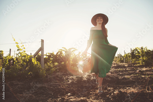  A beautiful lady walks in a field of vineyards in a long green dress and with a basket in her hands.