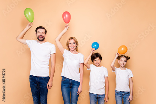 Young smiling family, bearded father, blonde mother, boy and girl wearing blue jeans and white T-shirts, standing in odrer of hierarchy, keeping air balls above their heads photo