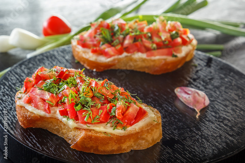 Bruschetta with fresh tomatoes and cheese on a black plate. Close-up