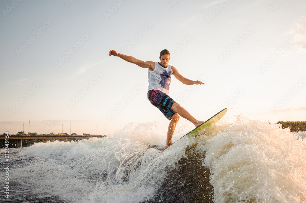 Young wakesurfer jumping on board riding down the river waves