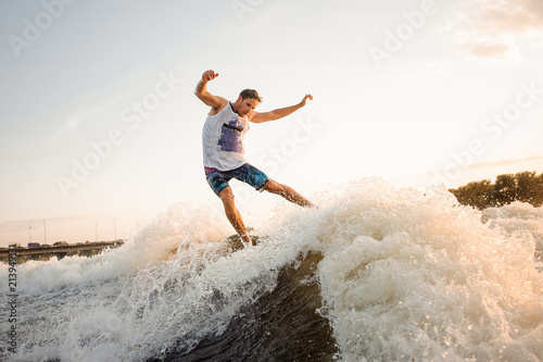 Young man riding on green wakesurf down the river waves