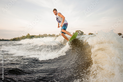 Active wakesurfer jumping on board riding down the river waves