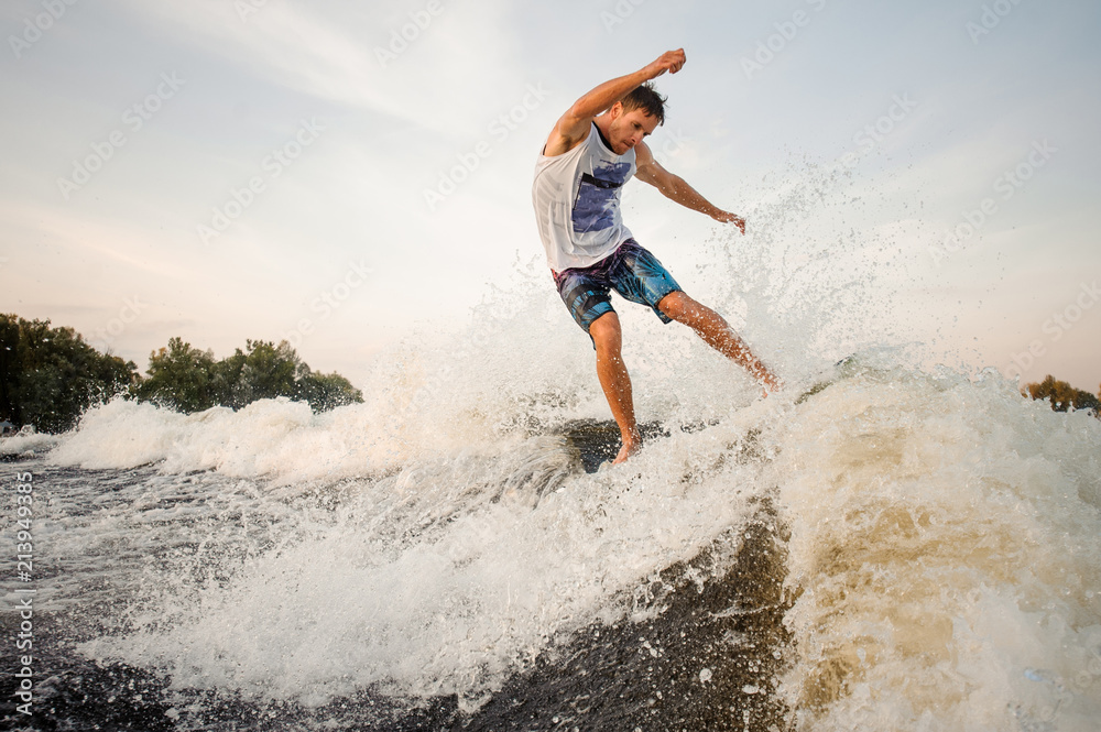 Young wakesurfer jumping and riding down the river on board
