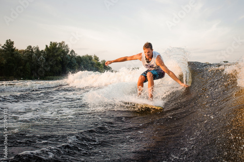 Muscular and strong wakesurfer riding down the river on board