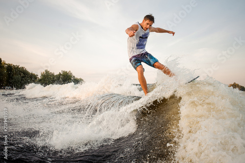 Muscular and strong wakesurfer jumping and riding down the river on board