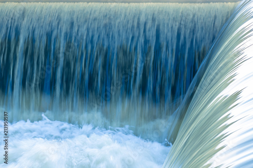 Small dam with motion of water flowing rapids. Seen as lines and patterns with foam.