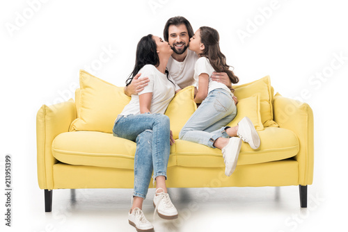 mother and daughter on yellow sofa kissing happy father isolated on white