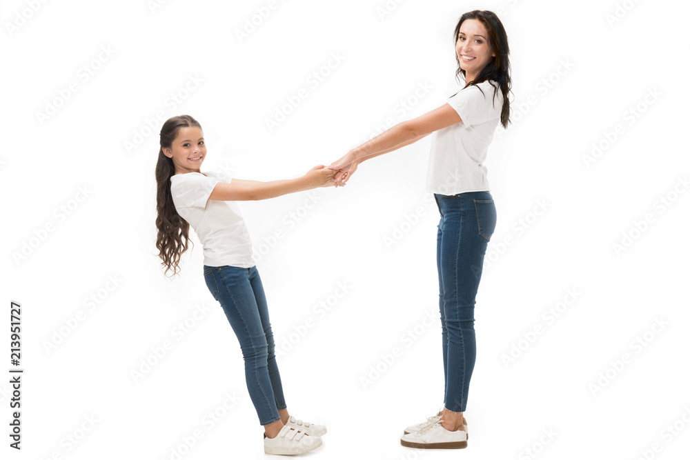 side view of happy mother and daughter in white shirts holding hands isolated on white side view of happy mother and daughter in white shirts holding hands isolated on white