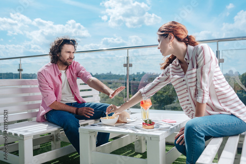 Lifting hand. Red-haired woman lifting her hand for trying fries of boyfriend while having lunch on summer terrace together © zinkevych