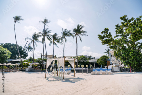 Wedding venue with minimal flower decoration on the beach, white cover chairs with blue stripes sash organza, long coconut palm tree background