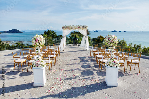 Beach wedding venue setting, panoramic sea view, blue sky, flower bouquet at the entrance of aisle, Wooden folder lawn chairs  arrangement