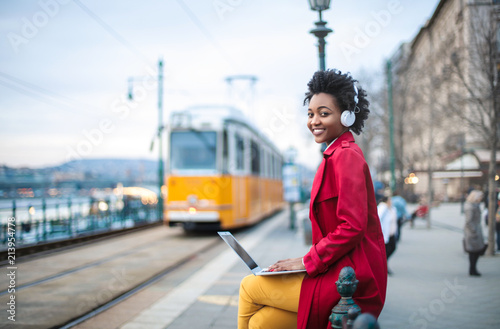 Woman sitting on the street, working with her laptop and listening music