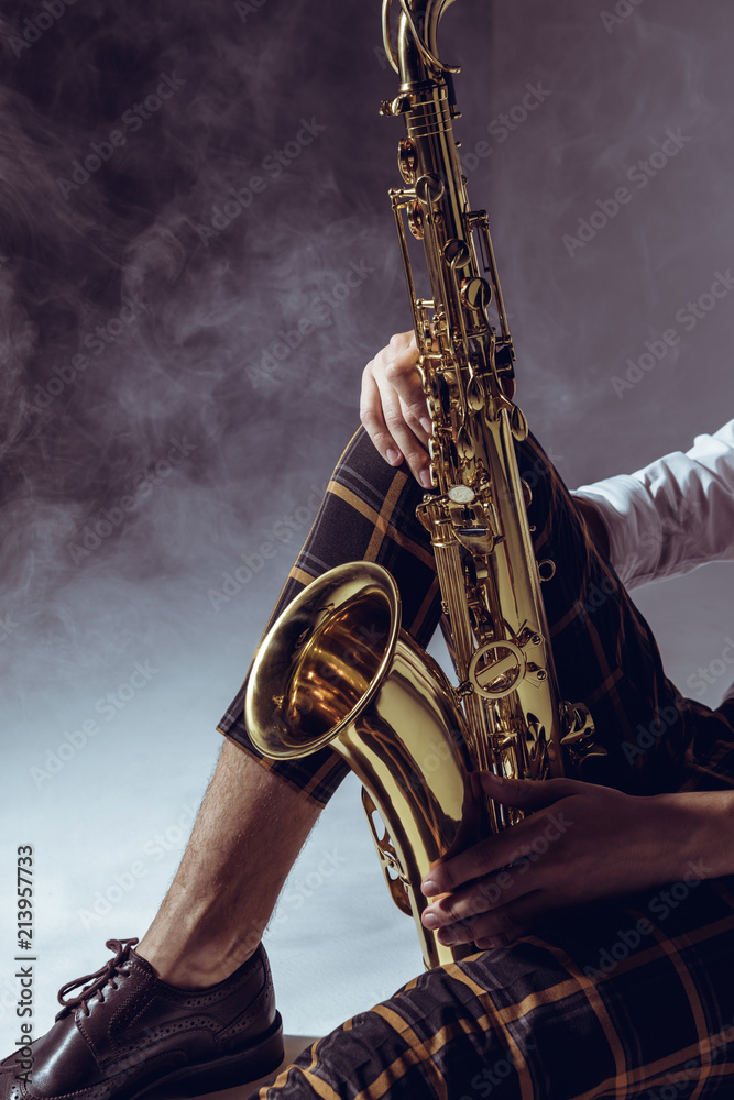 Obraz premium cropped shot of stylish musician holding saxophone in smoke on grey