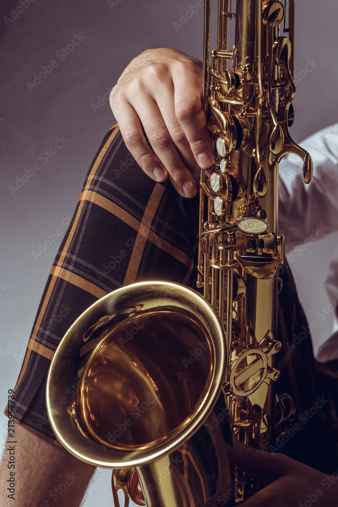 Obraz premium close-up partial view of stylish professional musician holding saxophone on grey
