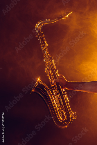 close-up partial view of young musician holding saxophone in smoke