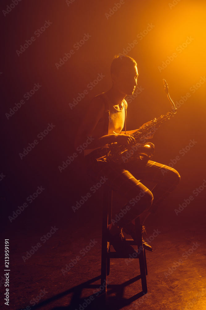 Naklejka premium young stylish jazzman sitting on stool and holding saxophone