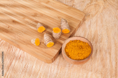 Turmeric powder and fresh turmeric on wooden background